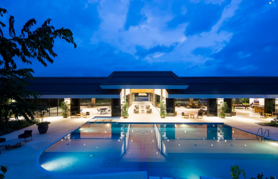 A modern hotel exterior with a pool and outdoor seating area at dusk