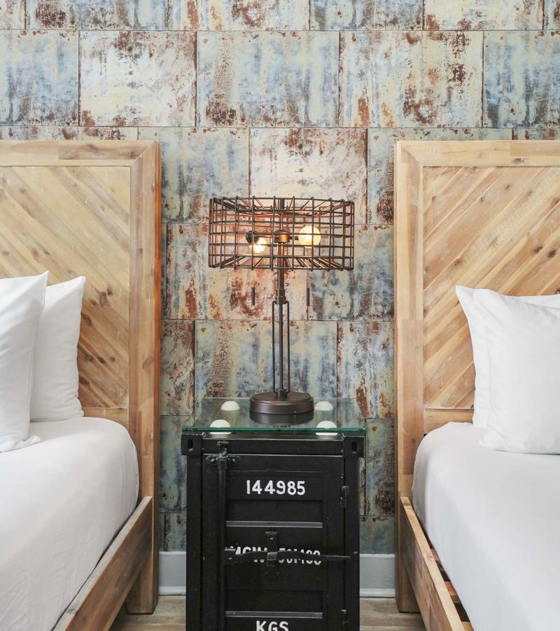A hotel room with two wooden beds, a metal lamp, and an industrial-style nightstand.