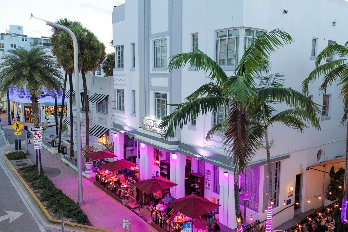 A white building with outdoor seating and palm trees in front of it