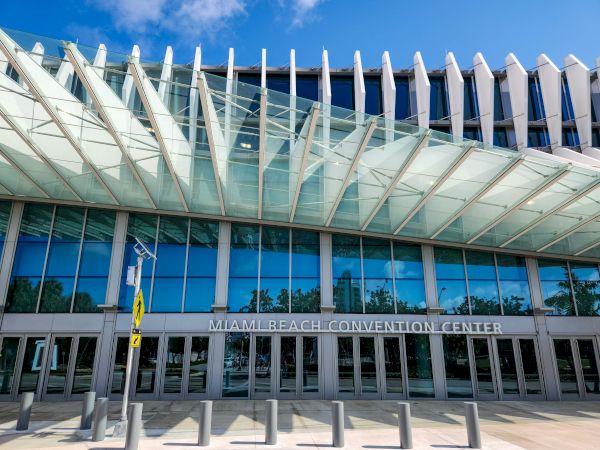 An event center with a modern glass facade and distinctive white vertical fins, labeled &ldquo;Miami Beach Convention Center&rdquo; at the entrance.