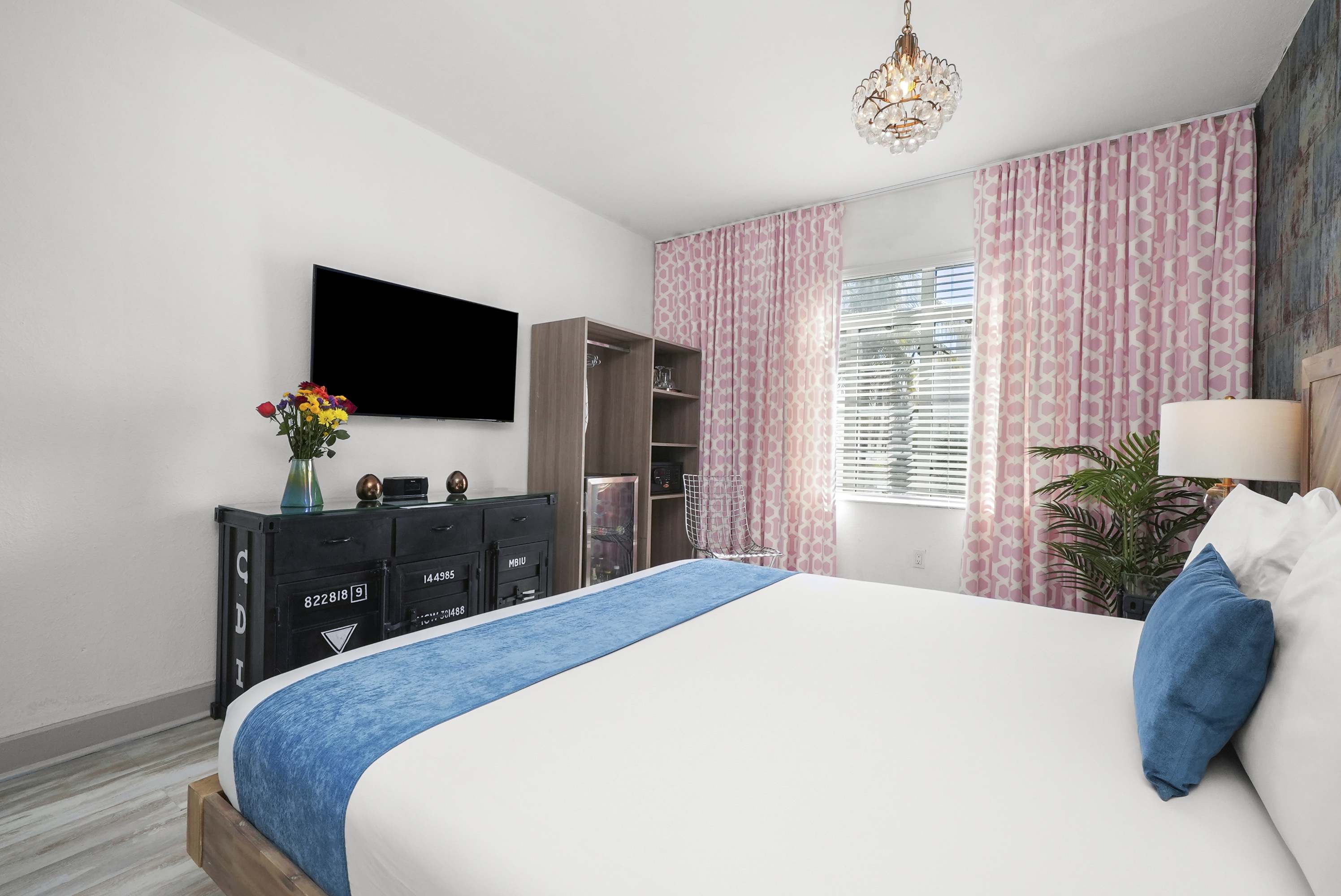 A wide-angle view of a guest room with a bed, TV, dresser, and window.