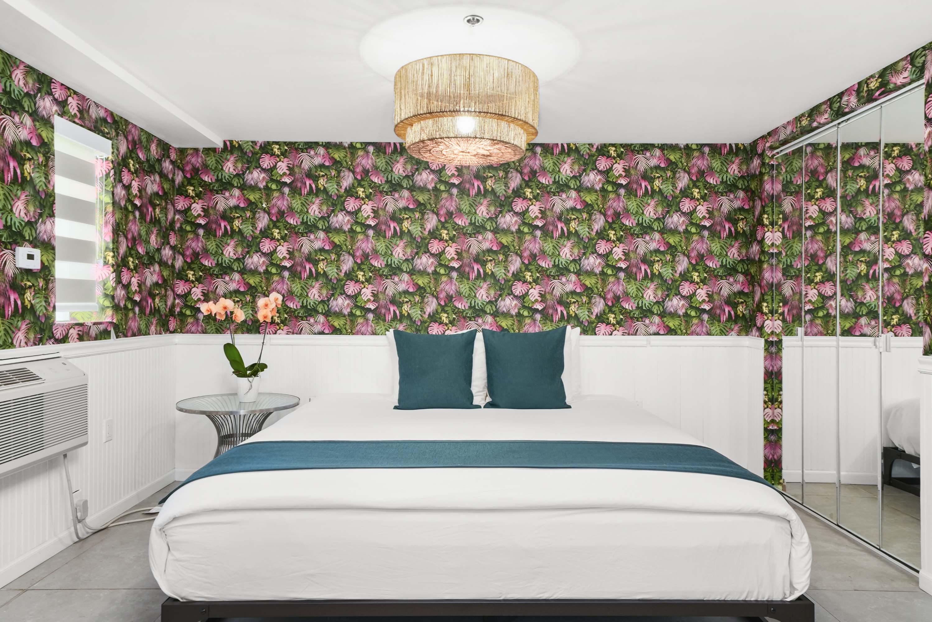 A hotel room with a large bed, floral wallpaper, and a wicker chandelier.