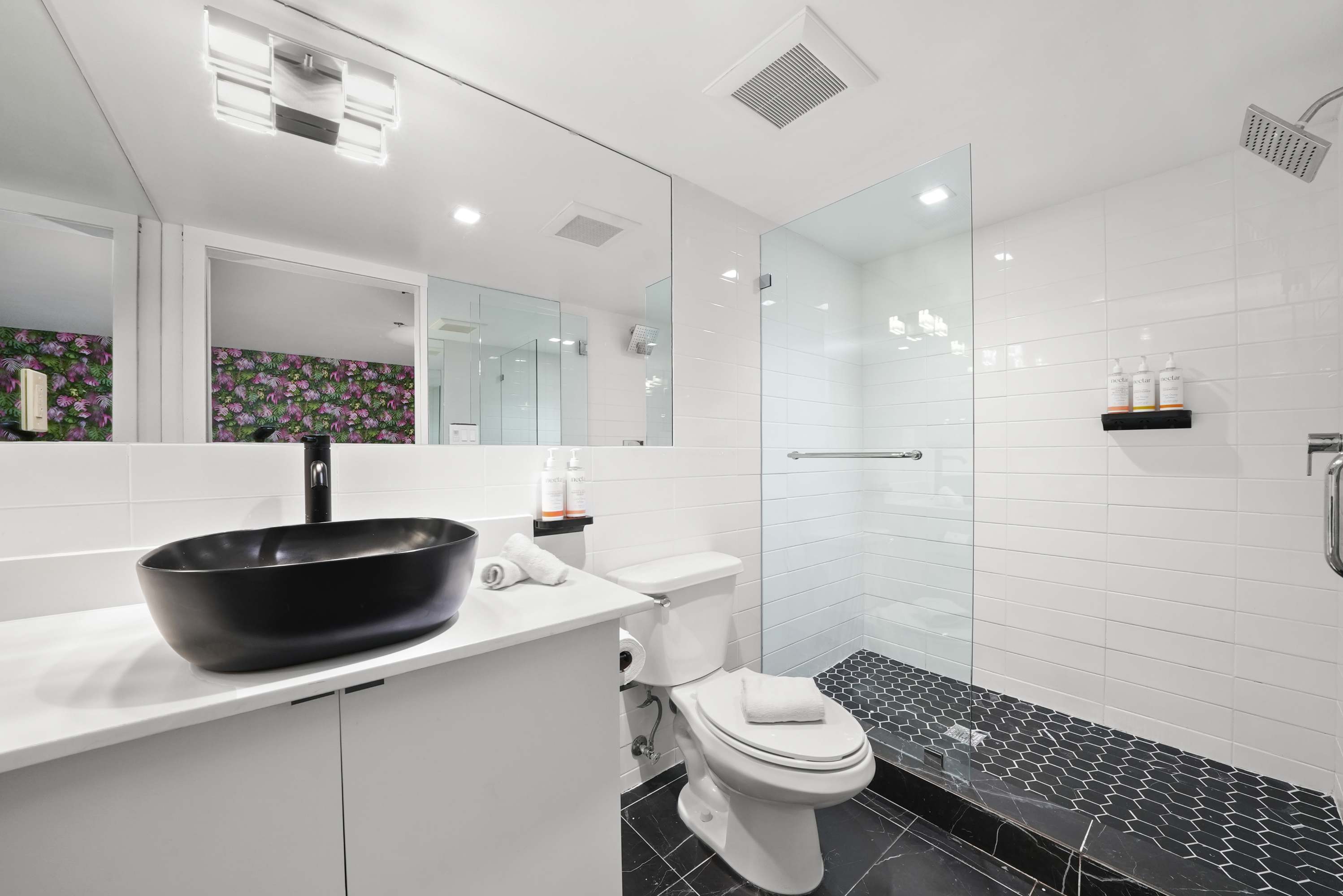 A modern bathroom with a black sink, white toilet, and glass-enclosed shower.