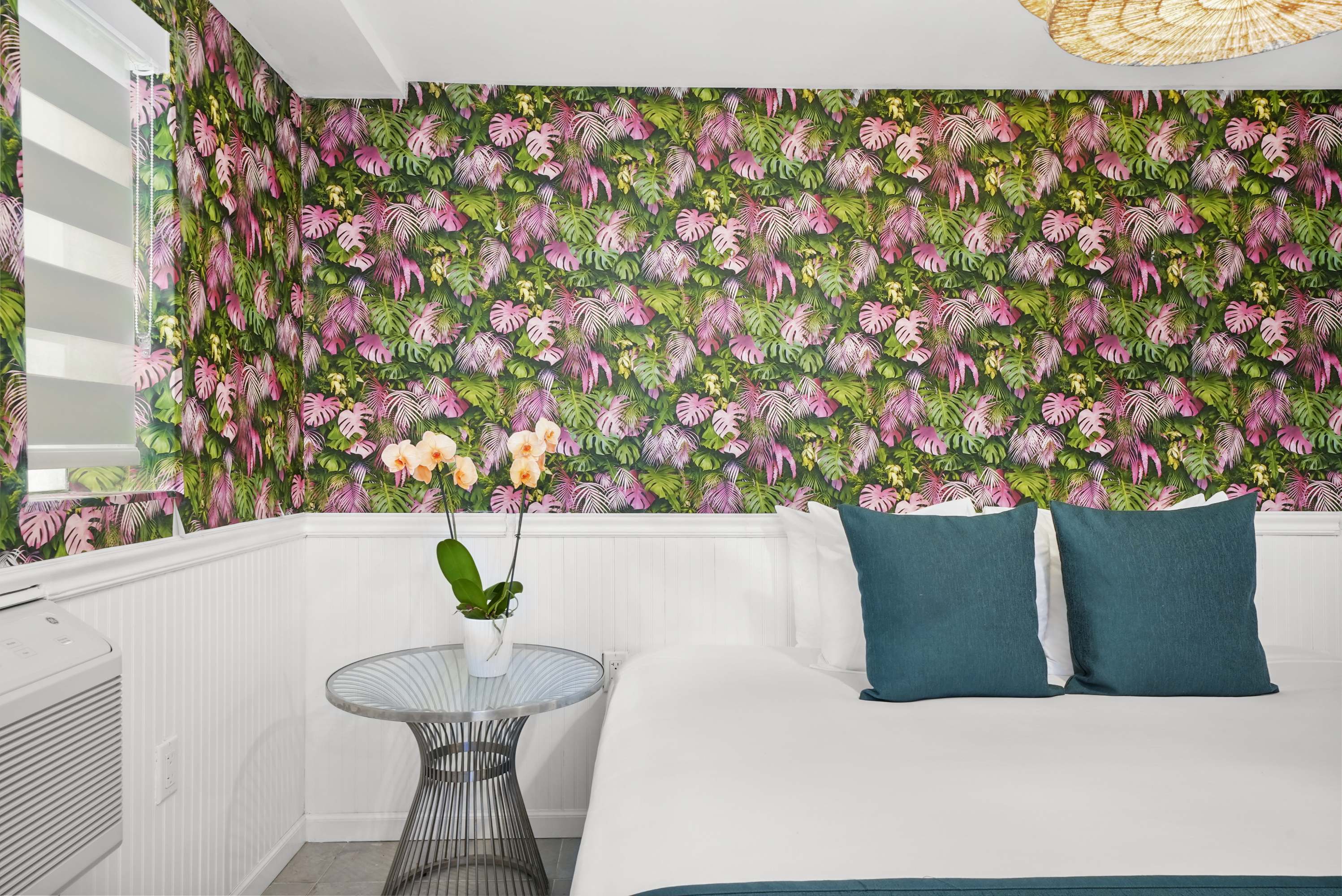 A bright and colorful guest room with a large bed, floral wallpaper, and a window