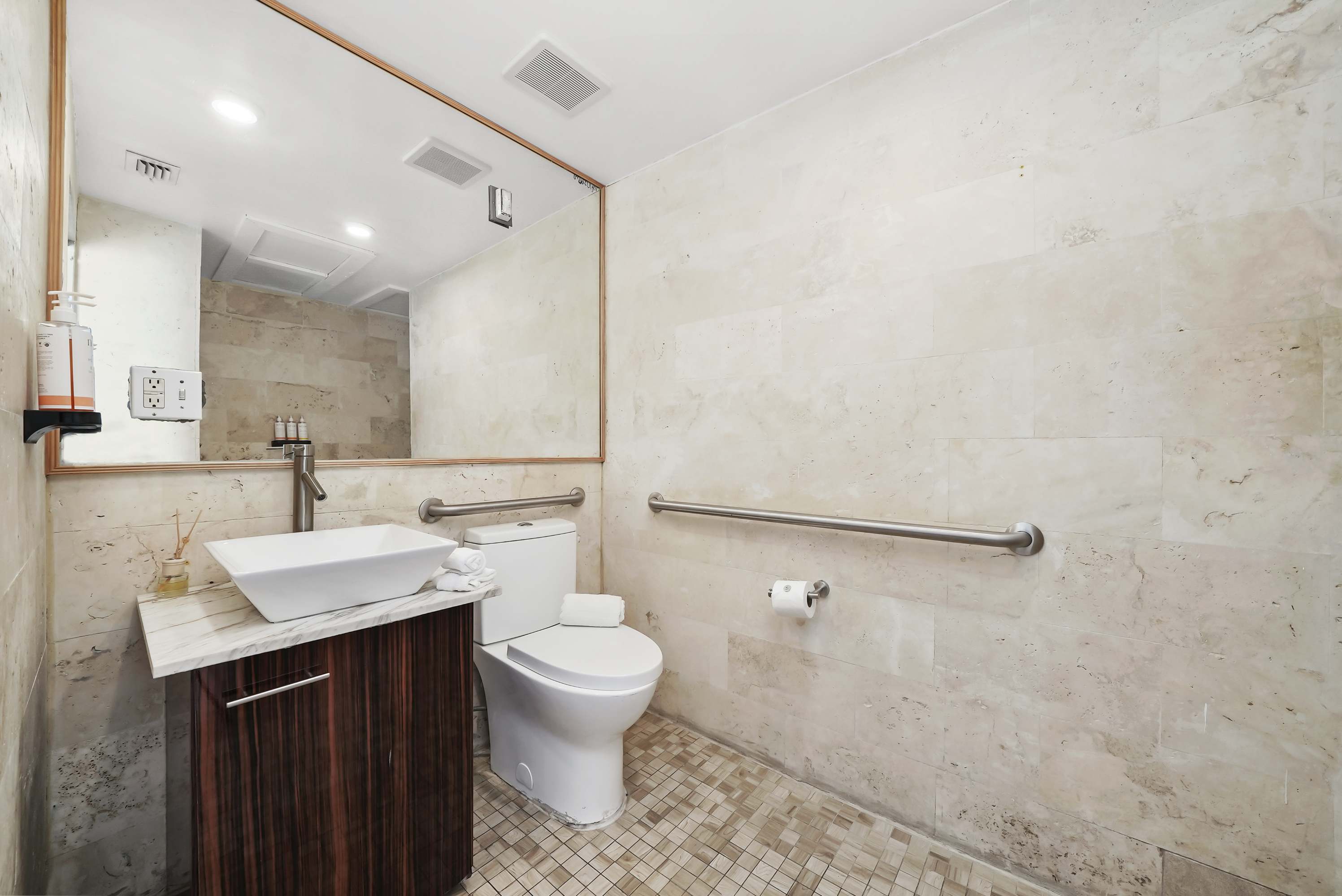 A clean and well-appointed bathroom with a large mirror, marble tiles, and grab bars.