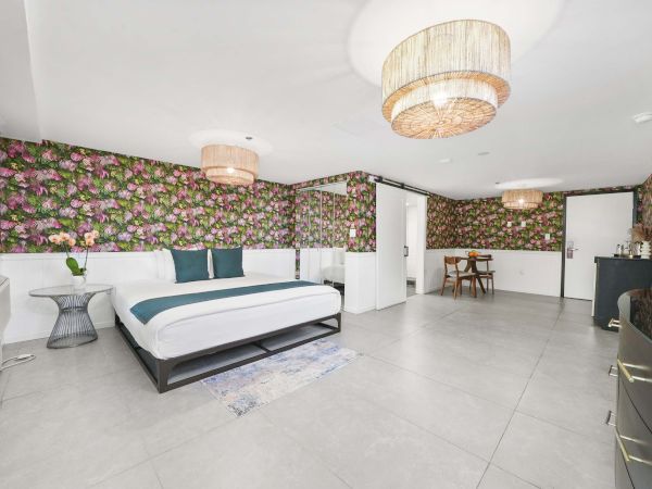 A modern, spacious bedroom with a floral wallpapered accent wall, a low-profile bed, stylish side tables, and a seating area in a well-lit, contemporary space.