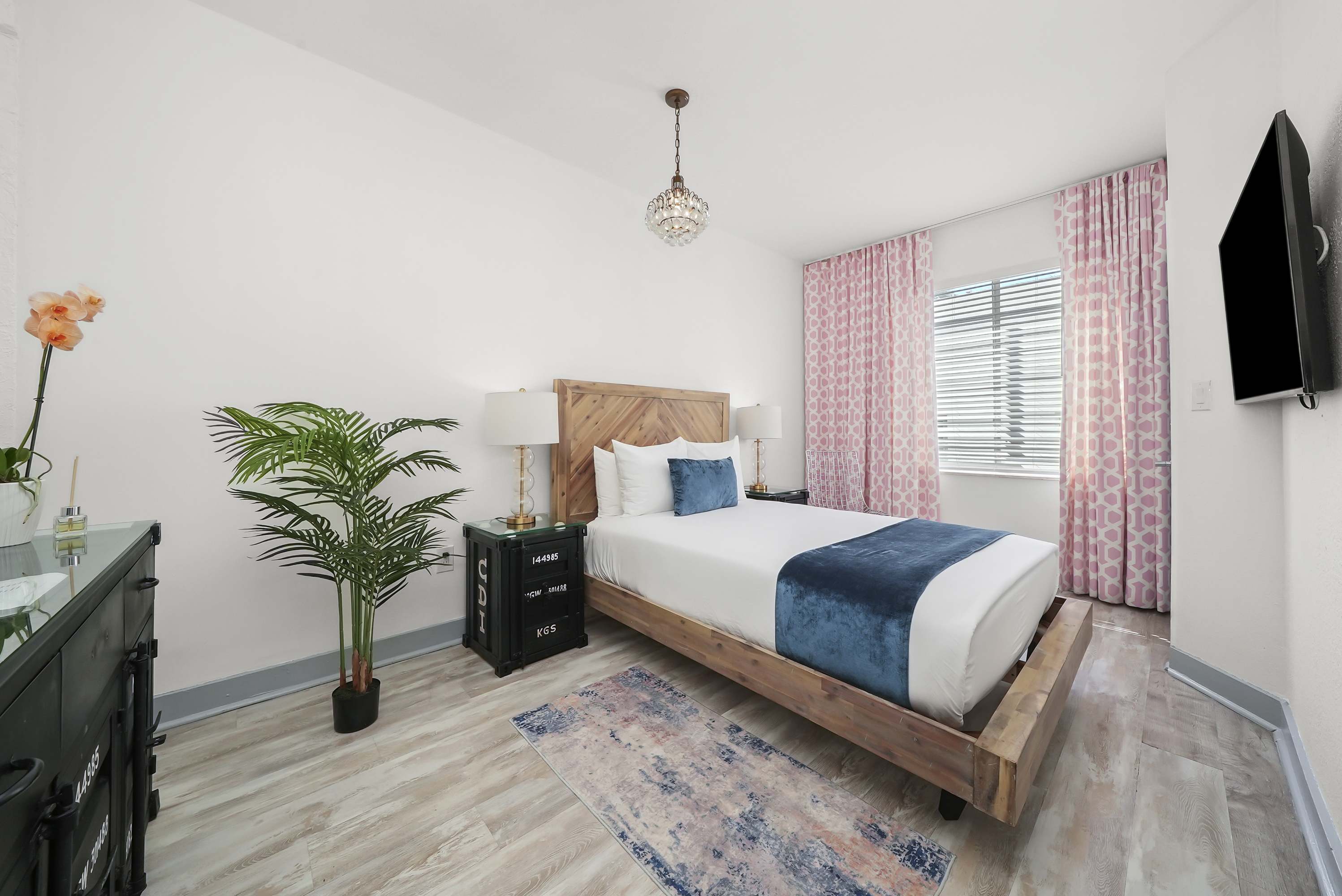 A neatly arranged hotel room with a wooden bed frame, white bedding, and blue accents.