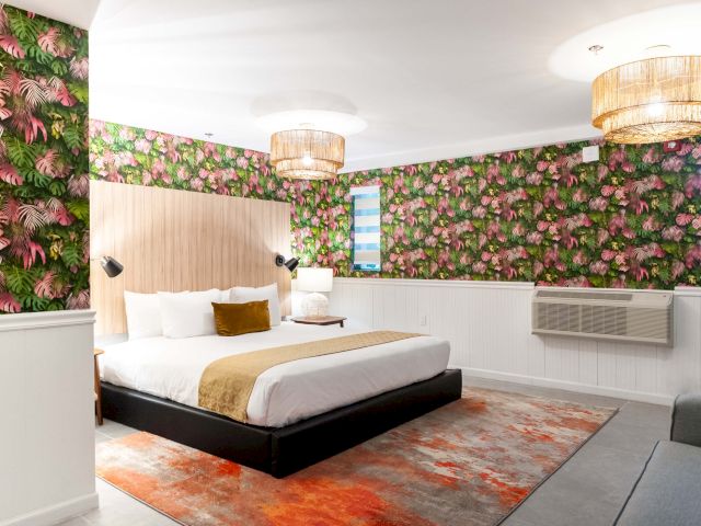 A wide view of a hotel room with a large bed, floral wallpaper, and modern lighting.