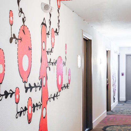 A hallway with whimsical pink and red cartoon figures and vines painted on the wall, creating a playful mural that winds along the corridor.