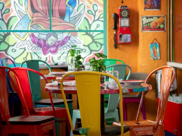A colorful dining area with a mural on the wall and plants on the tables.