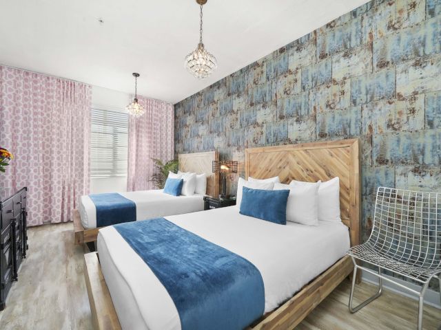 A wide view of a hotel room with two beds, a chandelier, and a patterned wall.