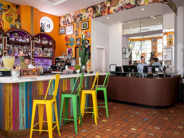 A colorful bar with stools, a counter, and a mirrored wall in the background.