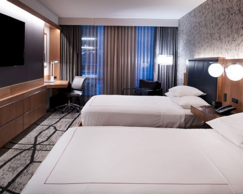 A hotel room with two twin beds, a desk, TV, and window with curtains.