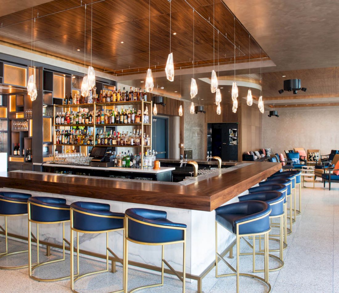 A modern bar with a wooden top, marble base, and blue stools with gold accents.