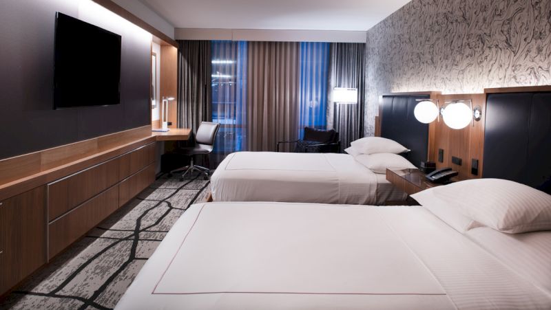 A modern hotel room with two beds, a desk, and a TV on the wall.